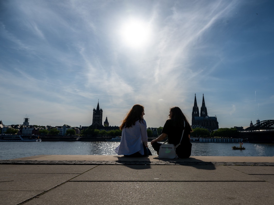 Zwei Frauen unterhalten sich am Rheinboulevard mit Blick zum Kölner Dom bei Sonnenschein.