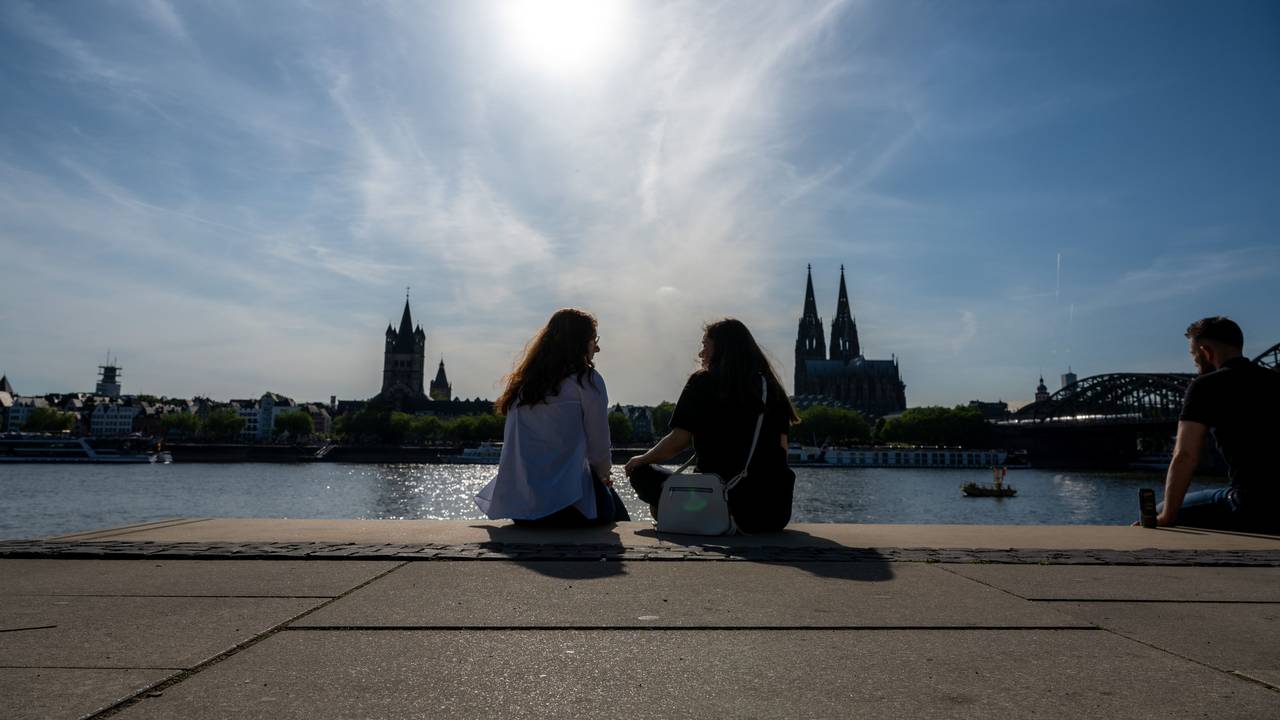 Zwei Frauen unterhalten sich am Rheinboulevard mit Blick zum Kölner Dom bei Sonnenschein.