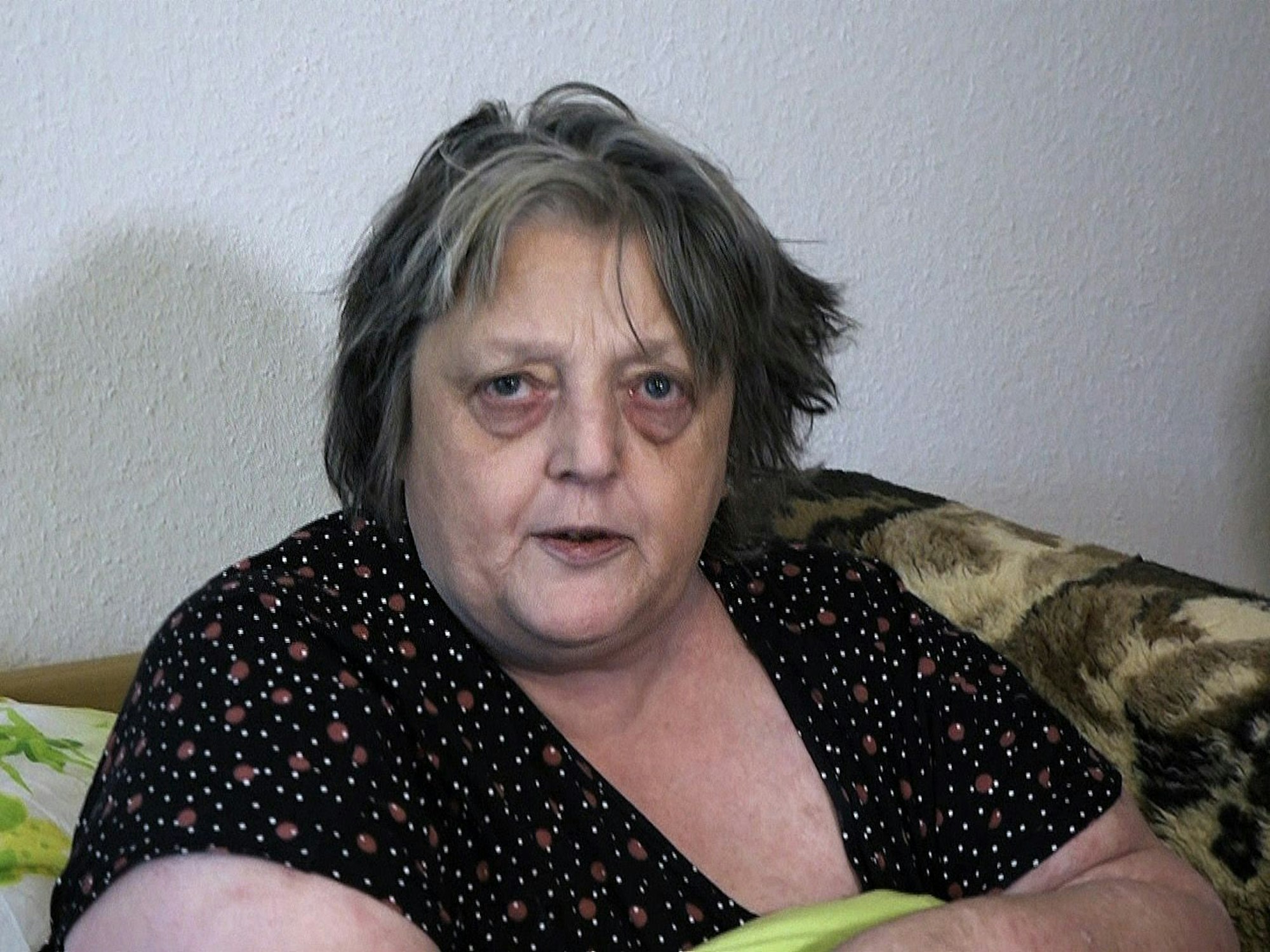 Gudrun sitzt auf dem Bett und guckt in die Kamera.