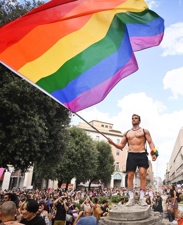 Menschen nehmen an der Pride-Parade in Bologna teil und ein Mann schwenkt eine große Regenbogenfahne.