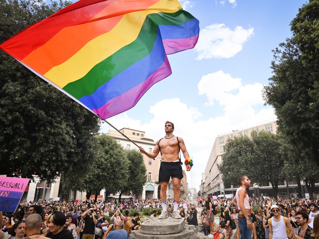 Menschen nehmen an der Pride-Parade in Bologna teil und ein Mann schwenkt eine große Regenbogenfahne.
