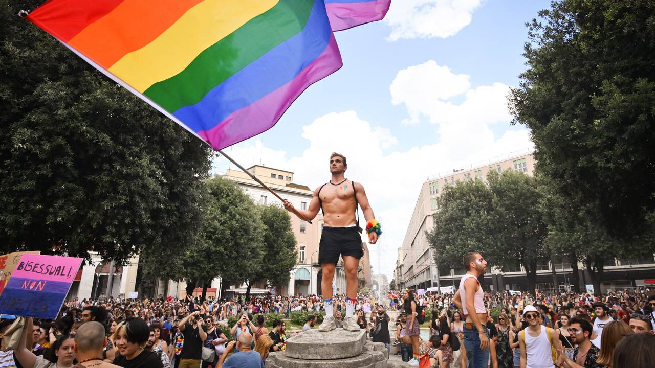 Menschen nehmen an der Pride-Parade in Bologna teil und ein Mann schwenkt eine große Regenbogenfahne.