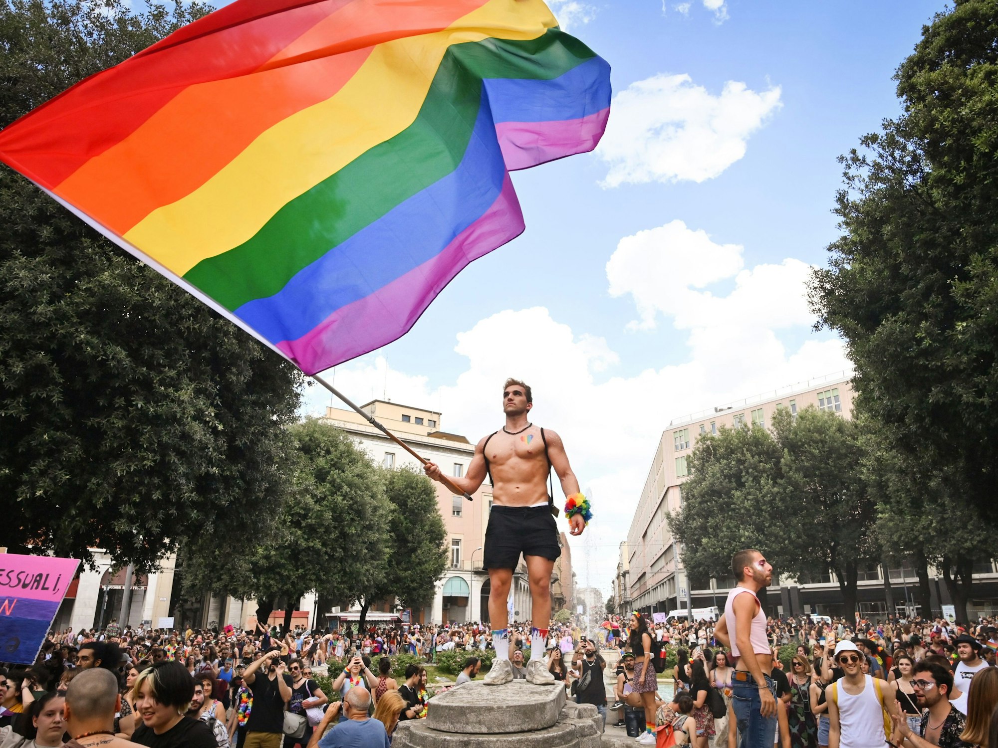 Menschen nehmen an der Pride-Parade in Bologna teil und ein Mann schwenkt eine große Regenbogenfahne.