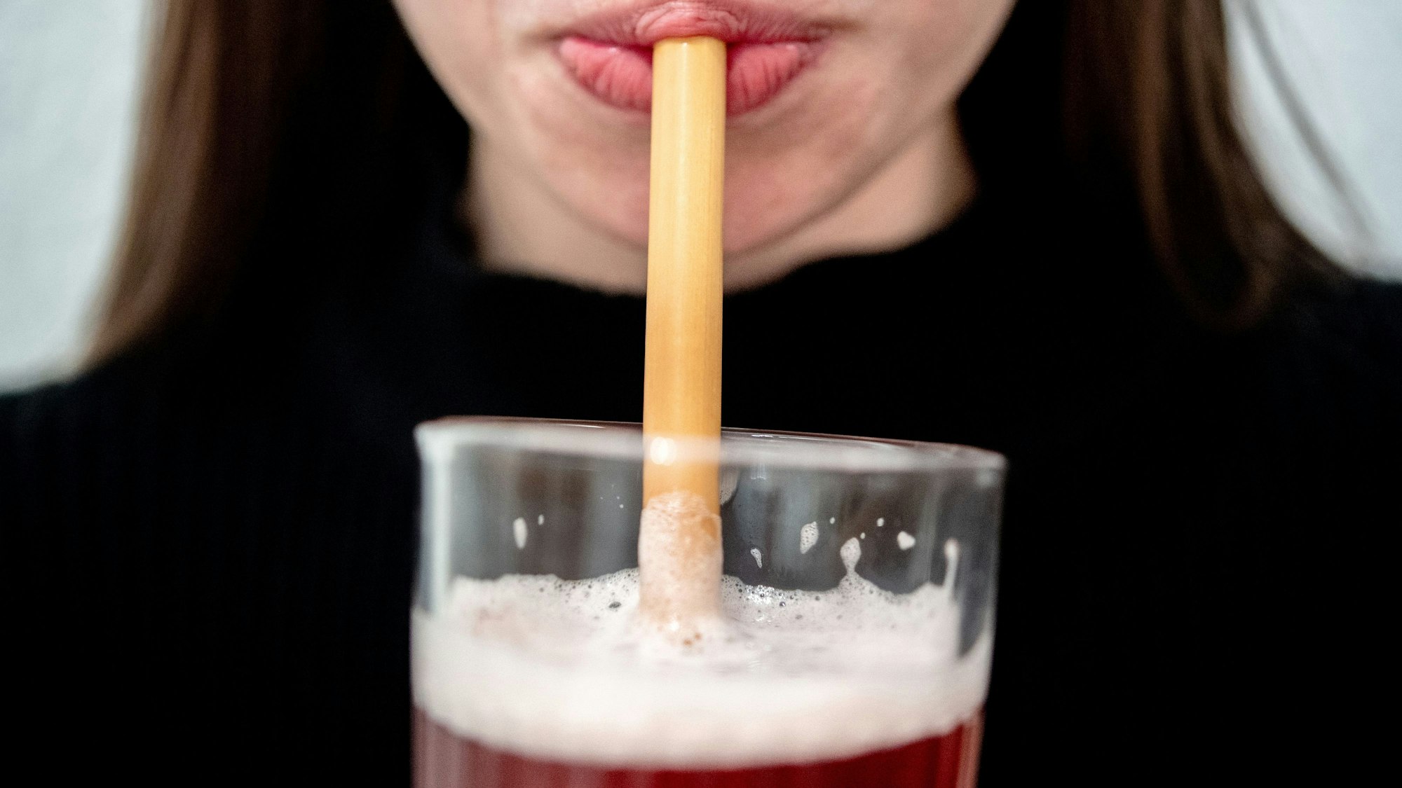 Eine junge Frau trinkt durch einen Trinkhalm aus Bambus aus einem Glas.