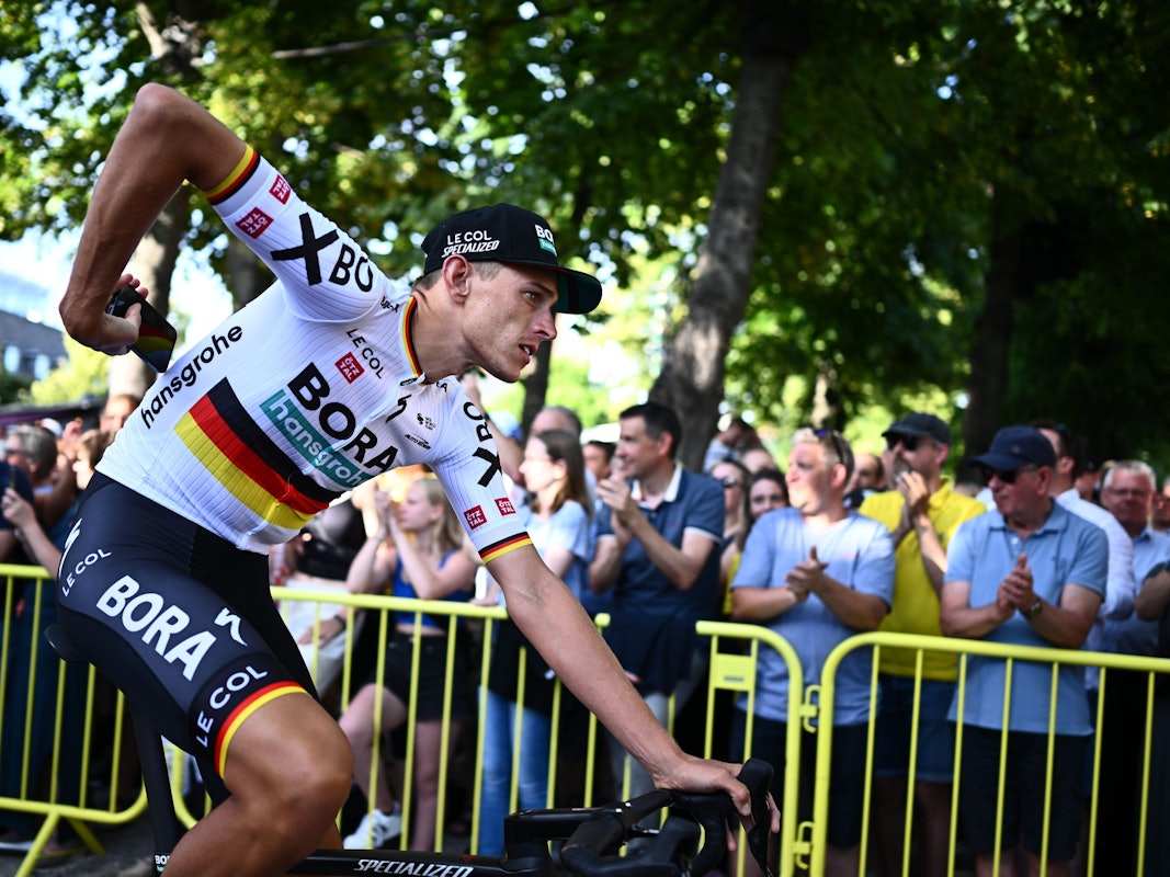 Nils Politt fährt mit einem Handy in der Hand an Zuschauern vorbei.