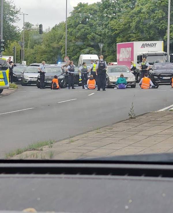 Demonstrierende sitzen auf der Straße vor zahlreichen Autos, die Polizei ist vor Ort.