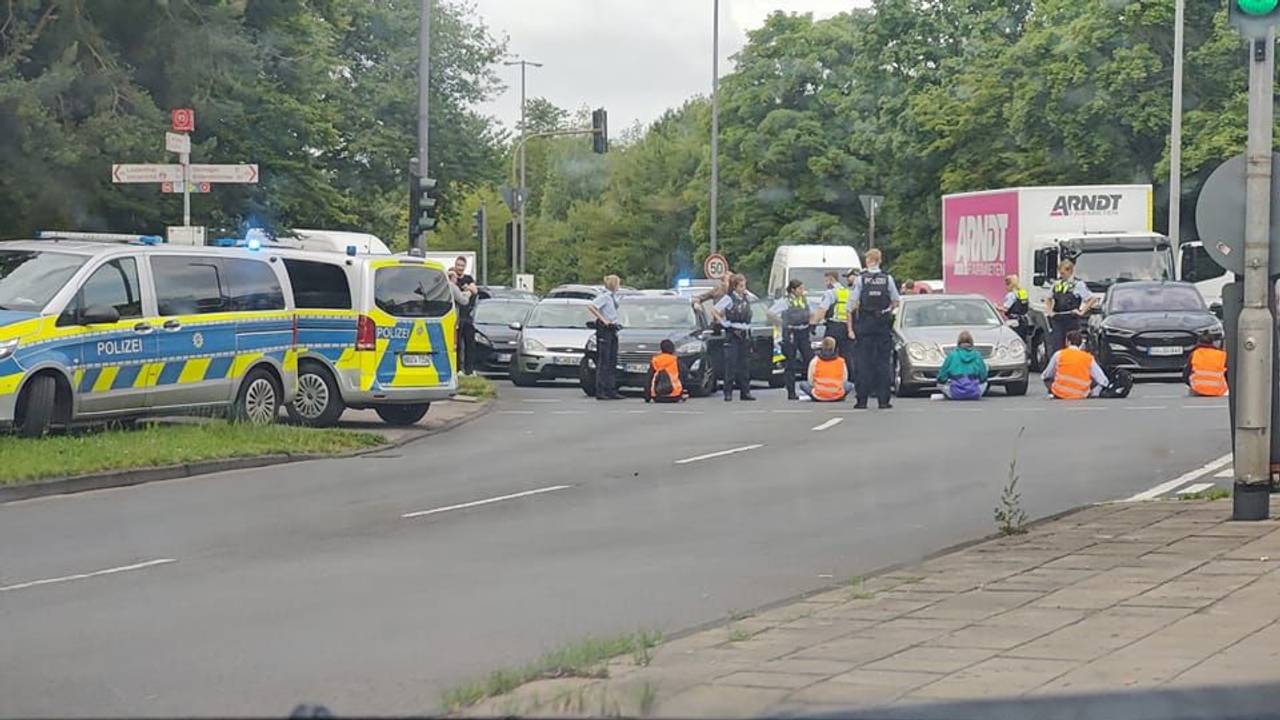 Demonstrierende sitzen auf der Straße vor zahlreichen Autos, die Polizei ist vor Ort.