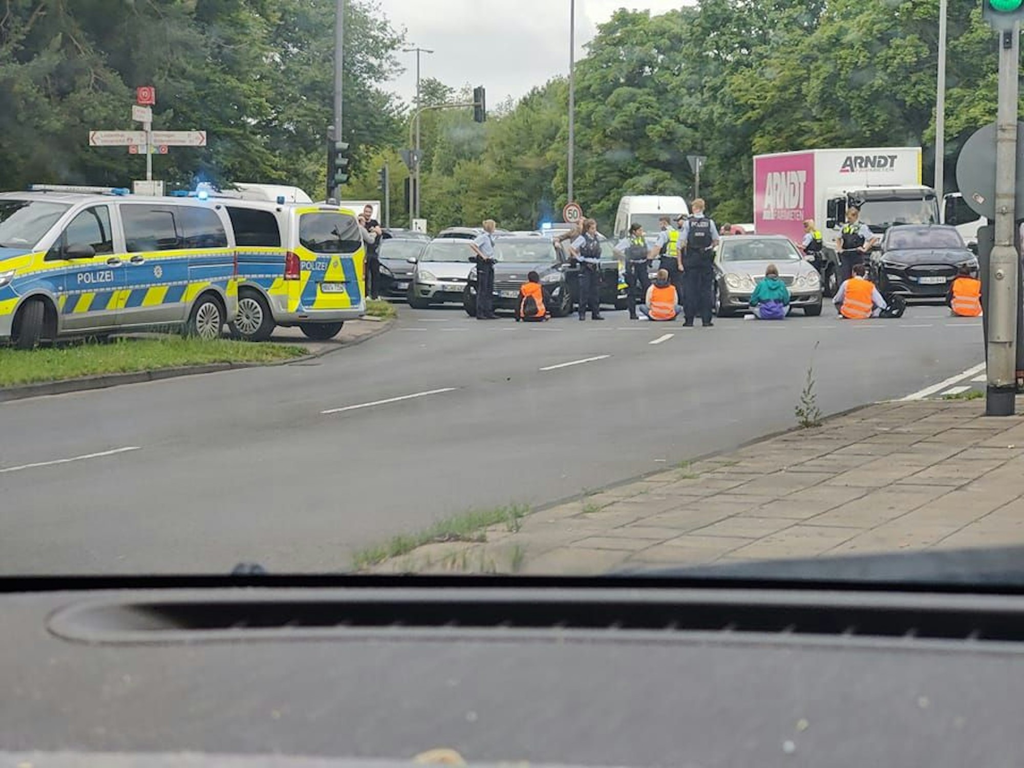 Demonstrierende sitzen auf der Straße vor zahlreichen Autos, die Polizei ist vor Ort.