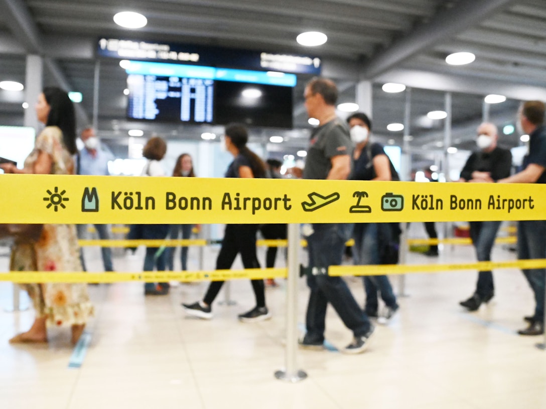 Passagiere laufen am Flughafen Köln/Bonn hinter einem Absperrband her.