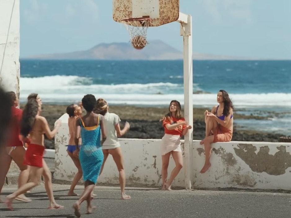 Screenshot aus dem Musikvideo „Provenza“ der kolumbianischen Sängerin Karol G. Mehrere Frauen spielen an der Promenade vor dem Meer Basketball.