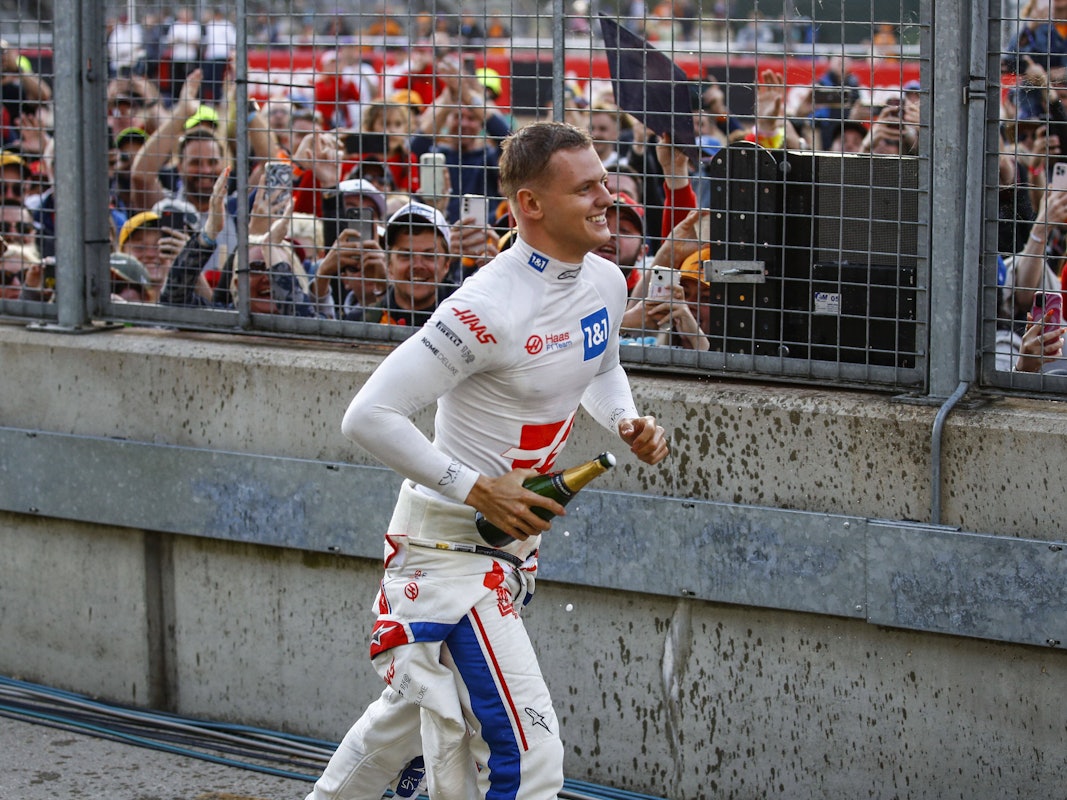 Mick Schumacher läuft mit einer Champagner-Flasche zu den Fans.