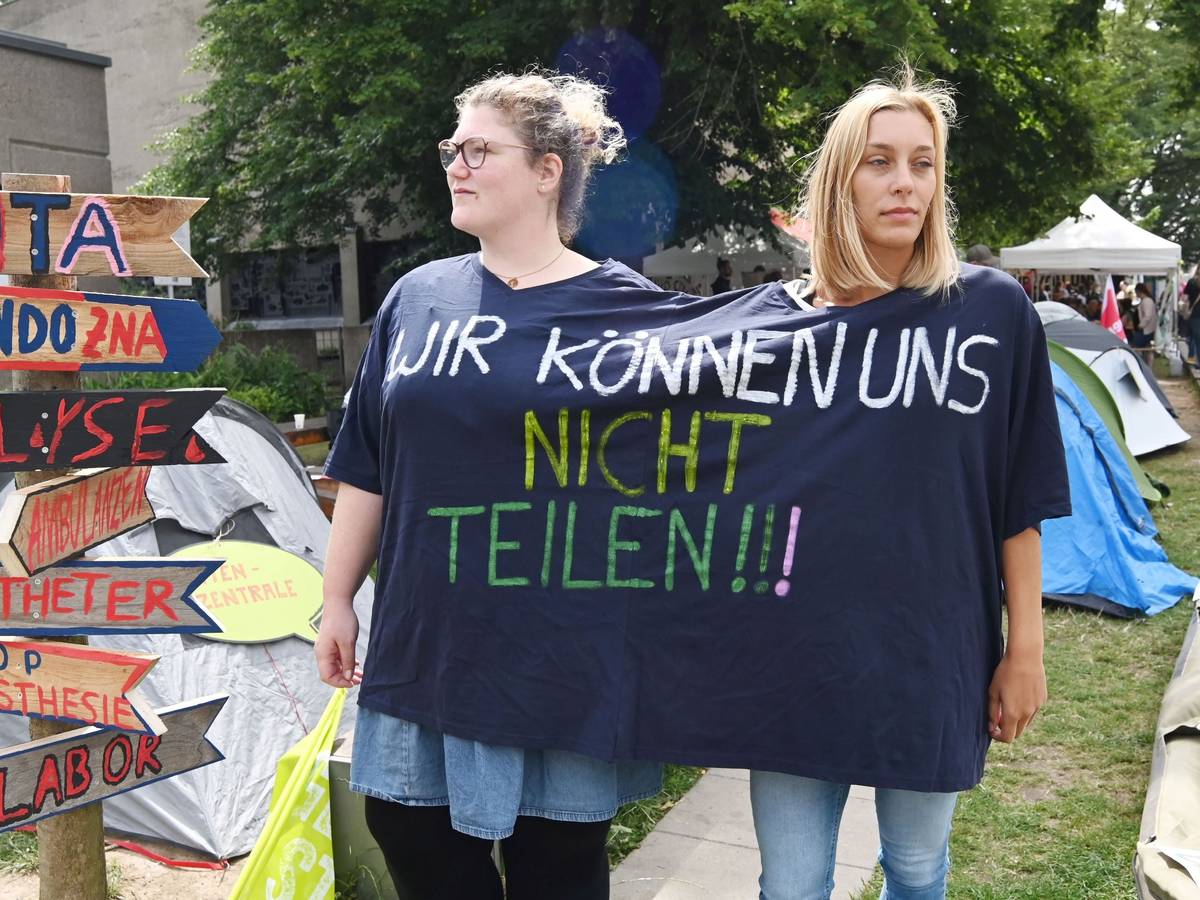 Zwei Streikende vor der Kölner Uniklinik in einem gemeinsam getragenen T-Shirt mit der Aufschrift "Wir können uns nicht teilen!"