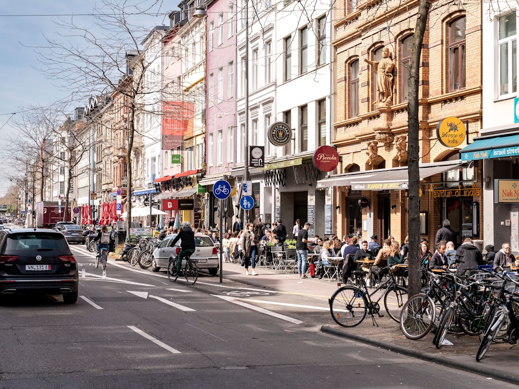 Menschen sitzen in Cafés am Straßenrand in Köln.