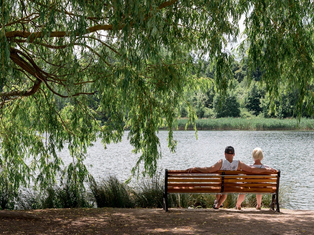 Ein Paar sitzt auf einer Bank in der Sonne an einem See.