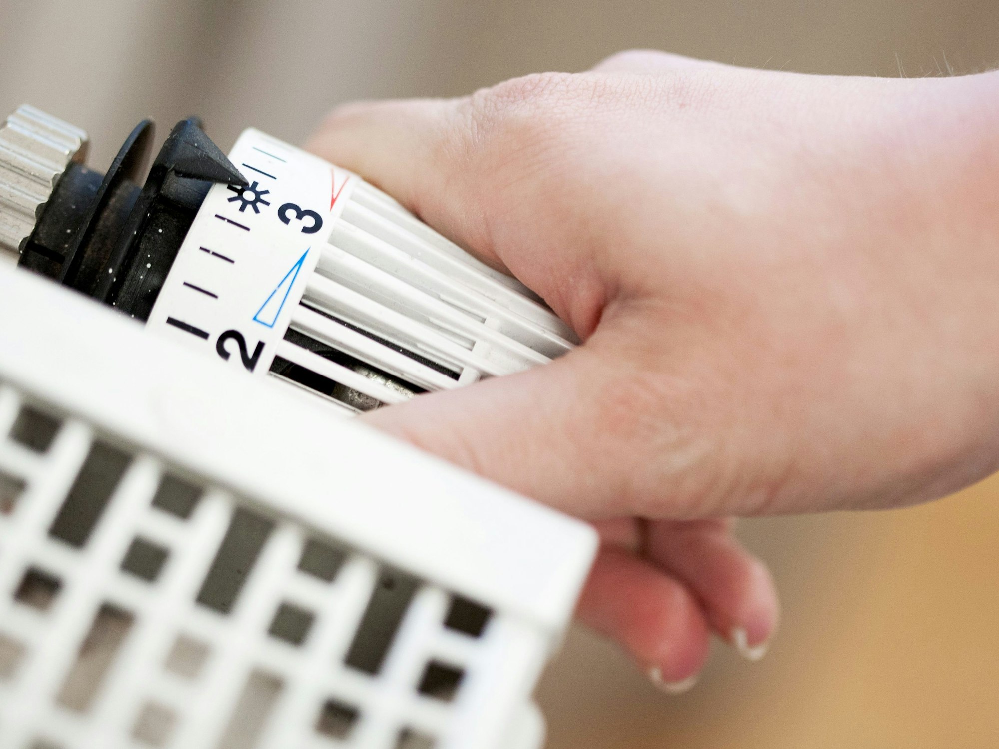 Eine Hand dreht am Temperaturregler eines Heizkörpers.