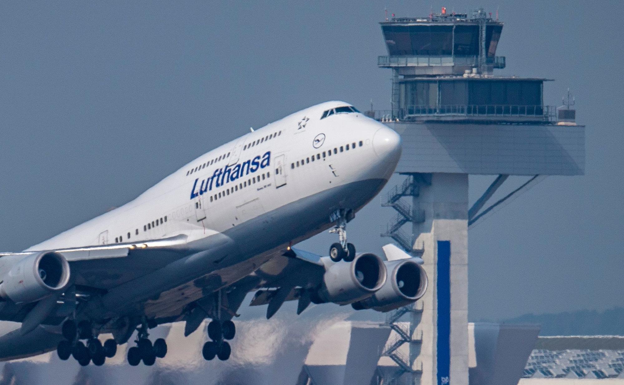 Eine Passagiermaschine vom Typ Boeing 747 der Lufthansa, hier eine Aufnahme von 2019, startet vor dem Tower des Flughafens Frankfurt zu einem Transatlantikflug. Lufthansa muss im Sommer 2022 weitere Flüge canceln.