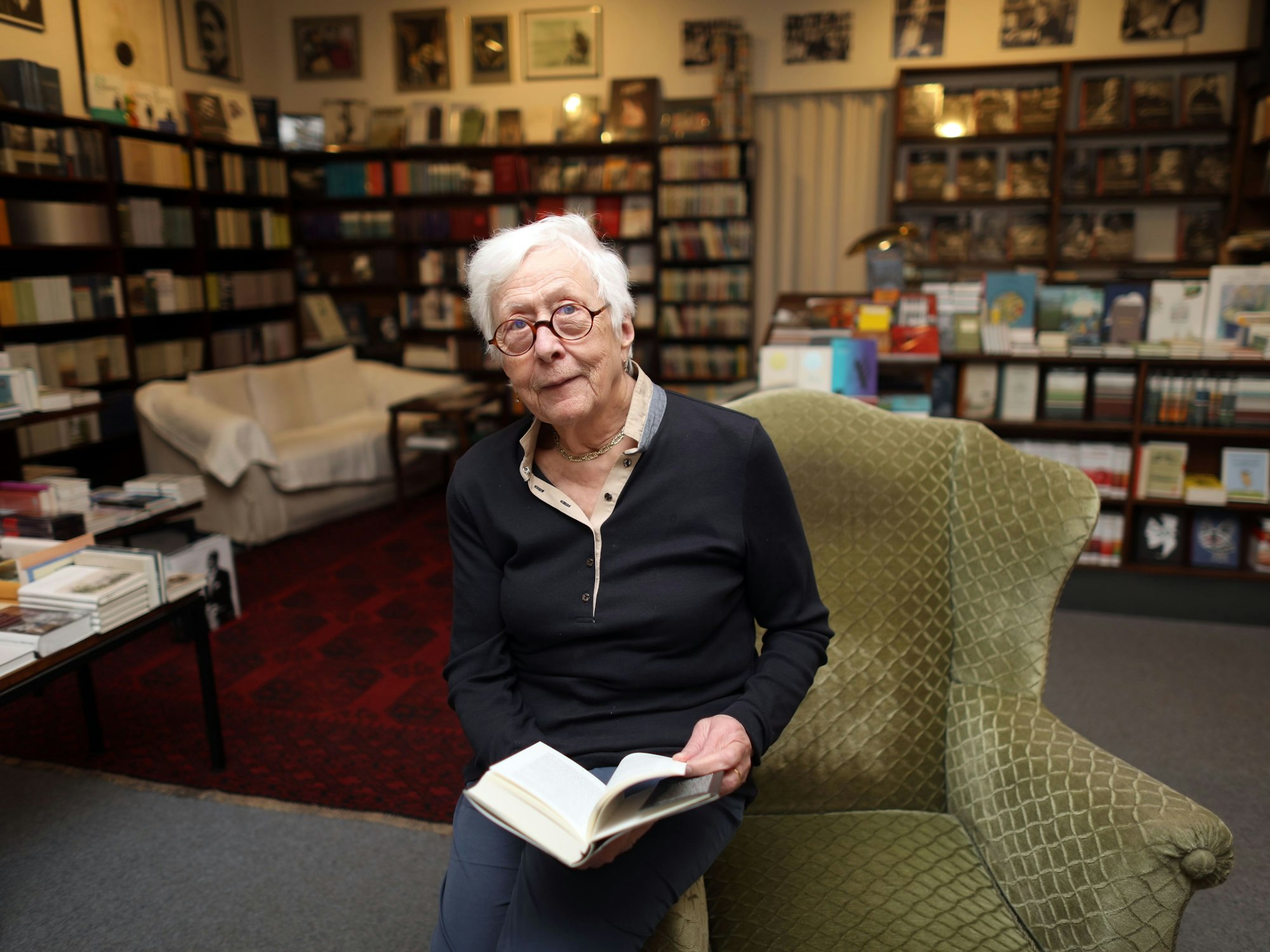 Hildegund Laaf sitz mit einem Buch auf der Lehne eines alten Ohrensessels in der Buchhandlung.
