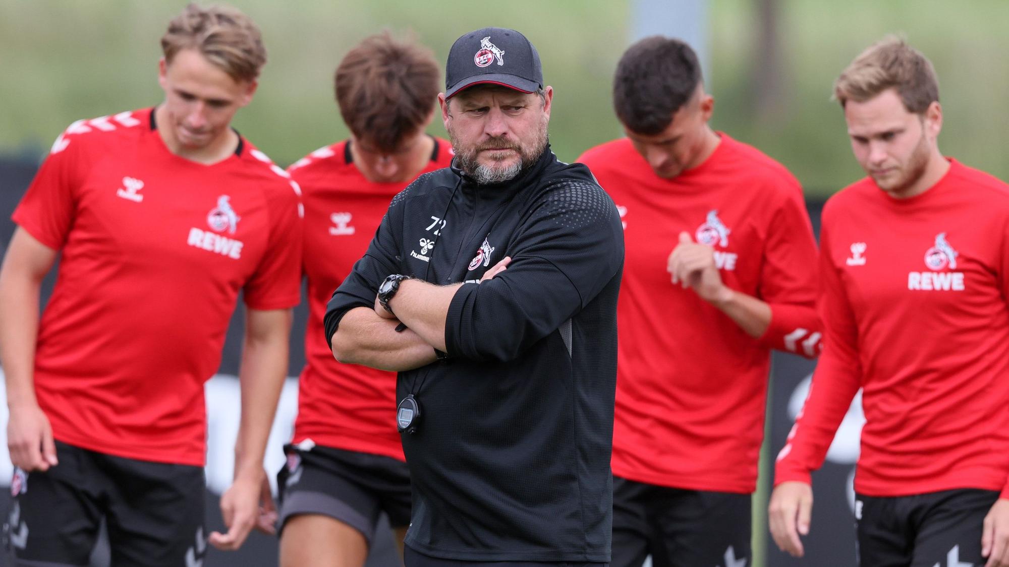 Steffen Baumgart steht im Training des 1. FC Köln mit verschränkten Armen auf dem Rasen.