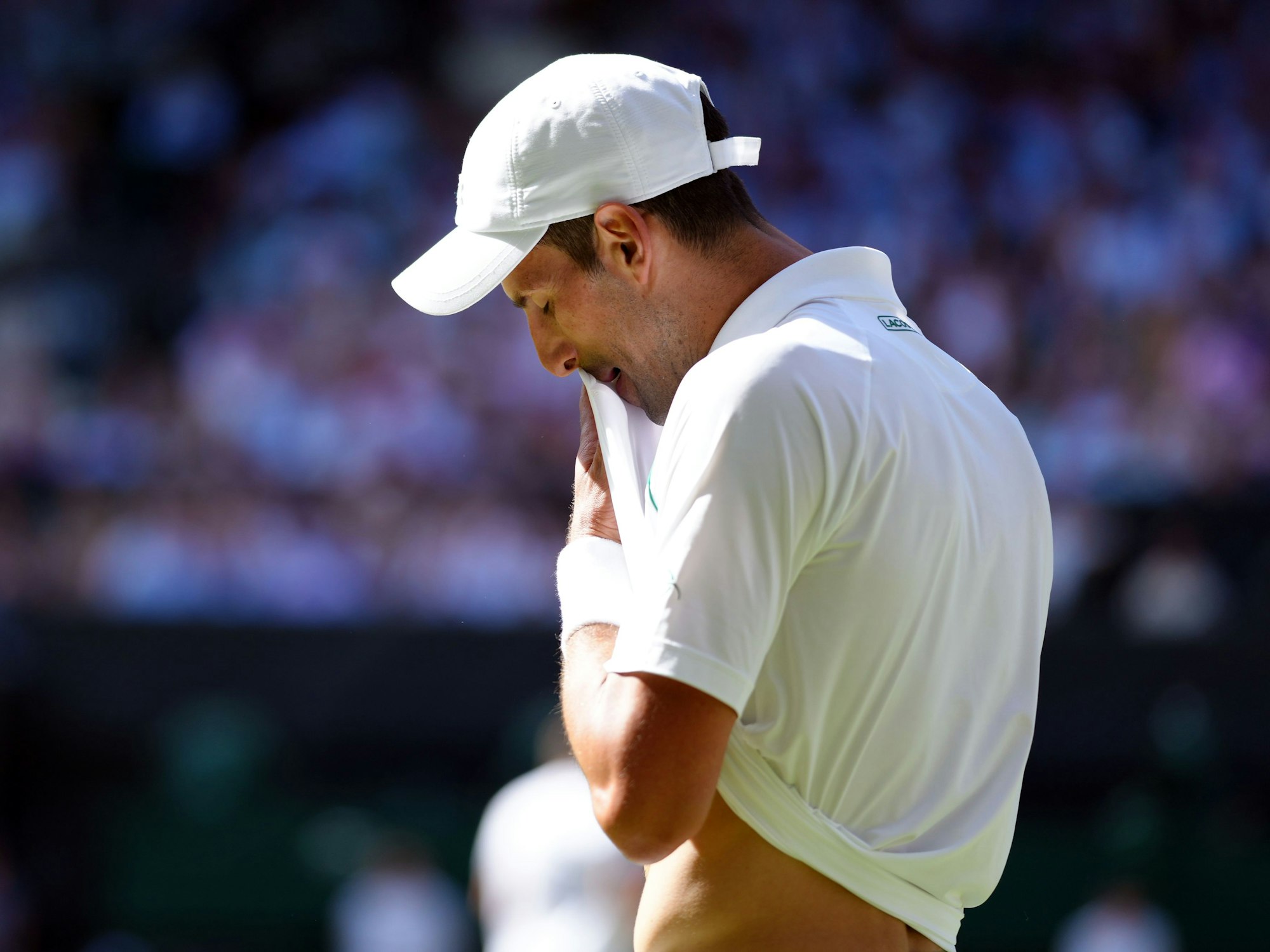 Novak Djokovic wischt sich mit seinem T-Shirt sein Gesicht ab.