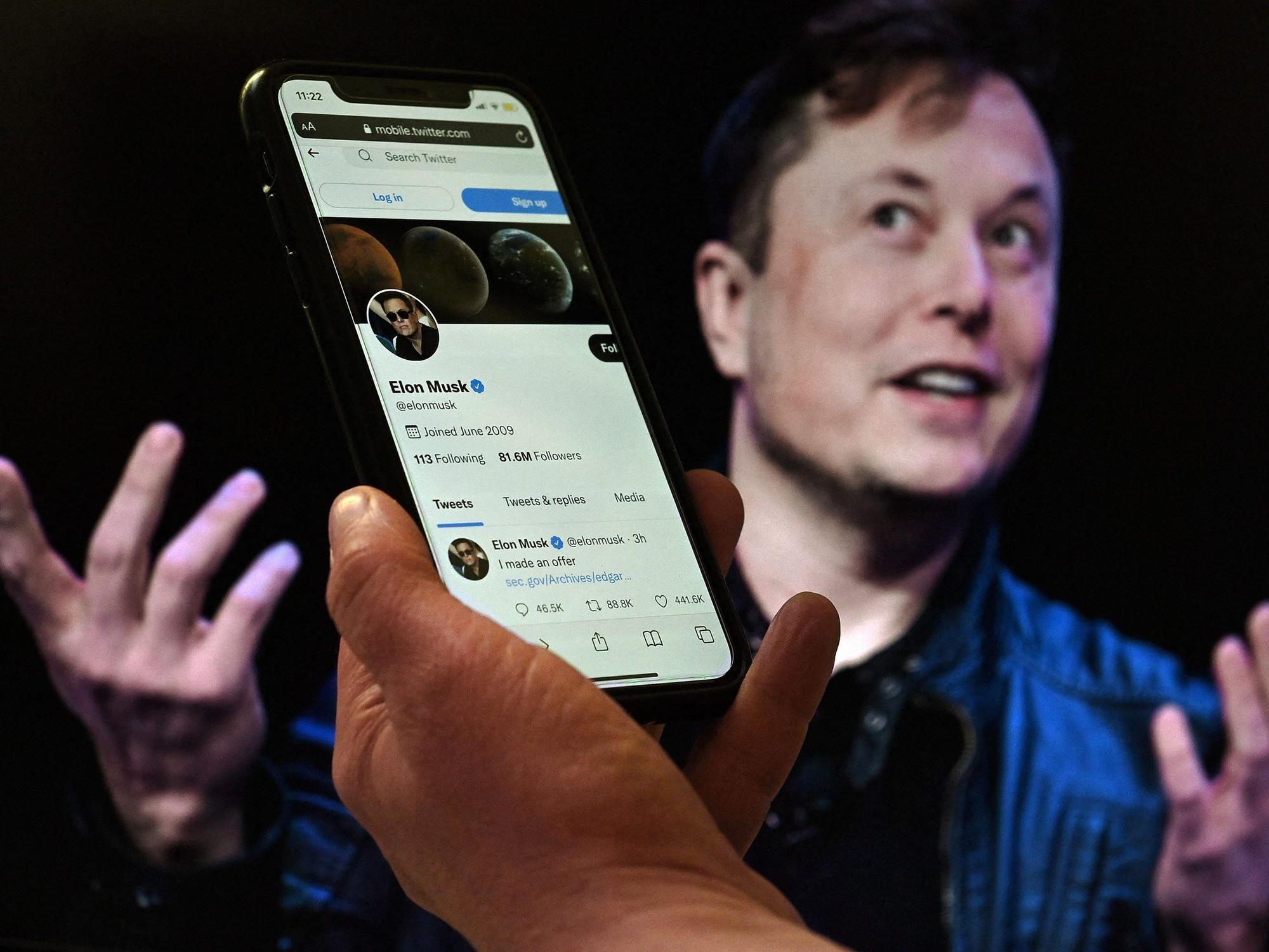 Der Deal zwischen Elon Musk und Twitter scheint geplatzt. Der Tech-Milliardär zweifelt die Unternehmenszahlen an. Twitter will im Notfall klagen. Das Foto eine Hand mit Smartphone, auf dem der Twitter-Account von Elon Musk. Im Hintergrund ist er selbst zu sehen.