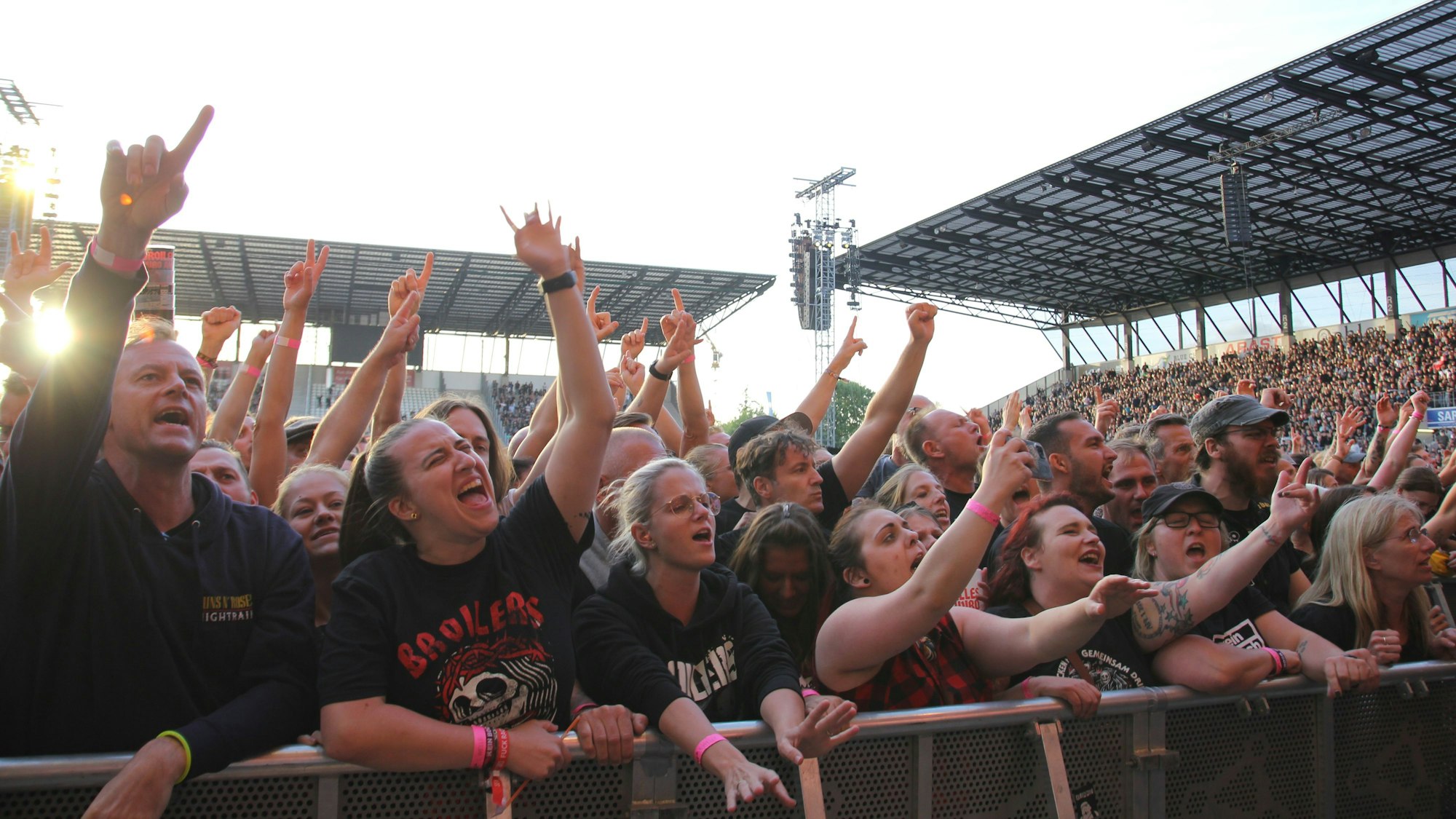 Konzertgäste stehen an einer Absperrung vor einer Bühne und singen mit.