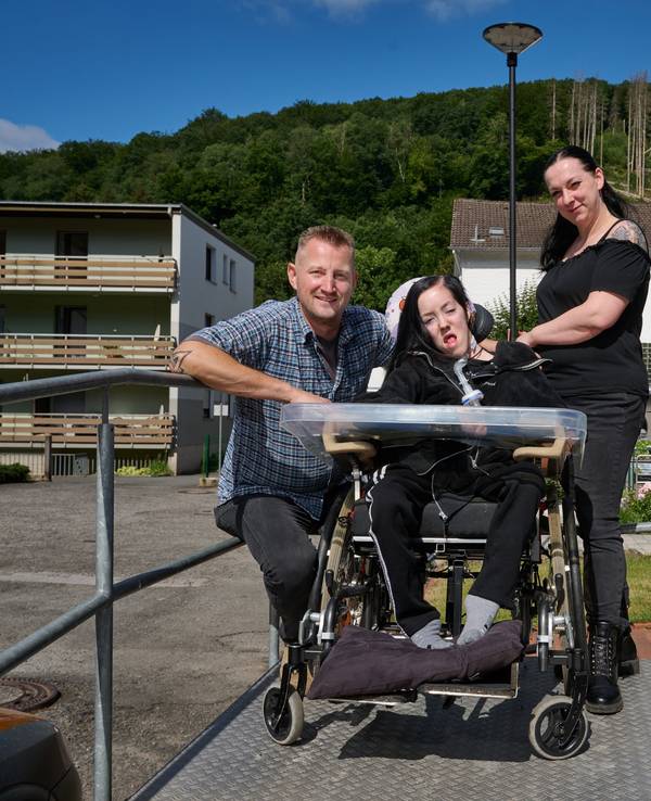 Dustin Raatz kniet neben dem Rollstuhl von Chantal und ihrer Mutter Bianca Caspari vor deren Haus. Mit einem tonnenschweren Bundeswehrfahrzeug aus dem Museum hatte Raatz das schwerkranke Mädchen während der schweren Flut im vergangenen Jahr gerettet und in Sicherheit gebracht, nachdem der letzte Akku ihres Beatmungsgerätes fast leer war.