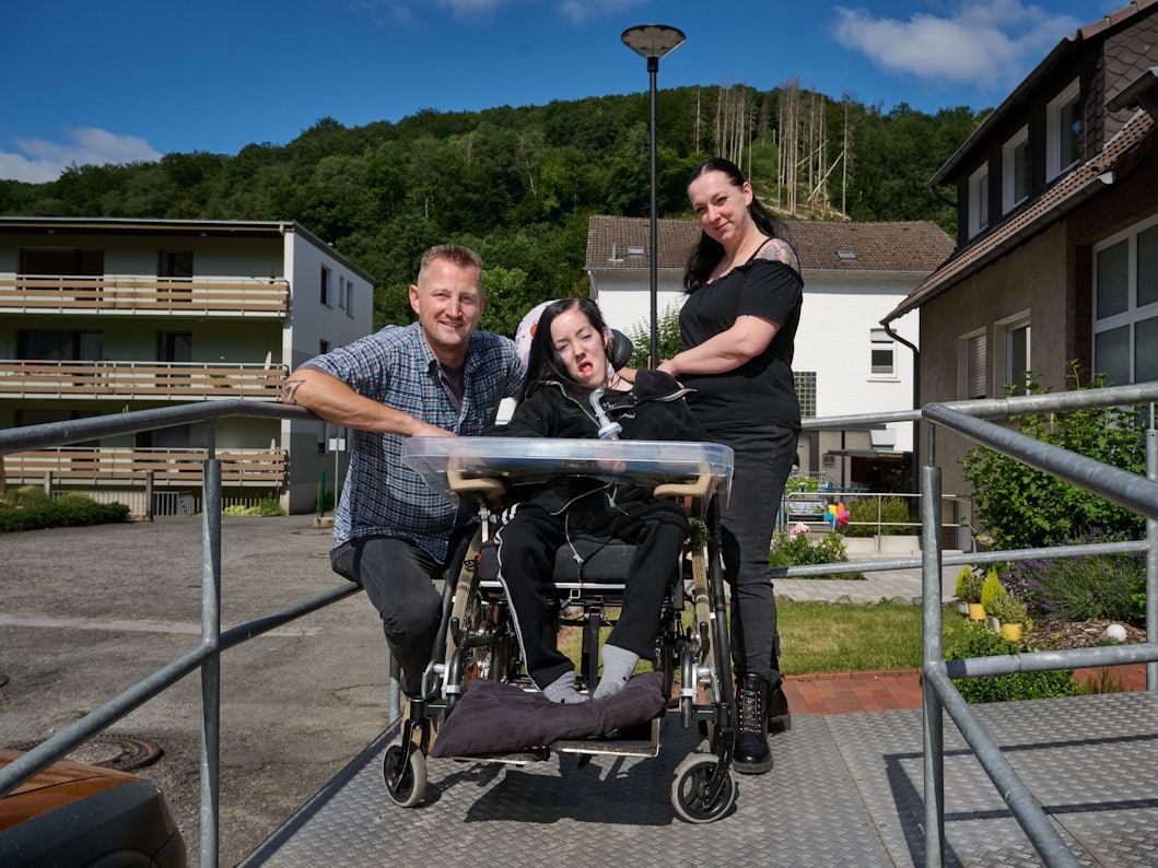 Dustin Raatz kniet neben dem Rollstuhl von Chantal und ihrer Mutter Bianca Caspari vor deren Haus. Mit einem tonnenschweren Bundeswehrfahrzeug aus dem Museum hatte Raatz das schwerkranke Mädchen während der schweren Flut im vergangenen Jahr gerettet und in Sicherheit gebracht, nachdem der letzte Akku ihres Beatmungsgerätes fast leer war.