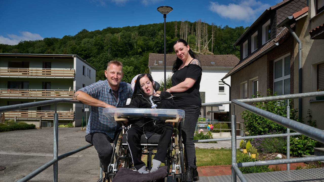 Dustin Raatz kniet neben dem Rollstuhl von Chantal und ihrer Mutter Bianca Caspari vor deren Haus. Mit einem tonnenschweren Bundeswehrfahrzeug aus dem Museum hatte Raatz das schwerkranke Mädchen während der schweren Flut im vergangenen Jahr gerettet und in Sicherheit gebracht, nachdem der letzte Akku ihres Beatmungsgerätes fast leer war.