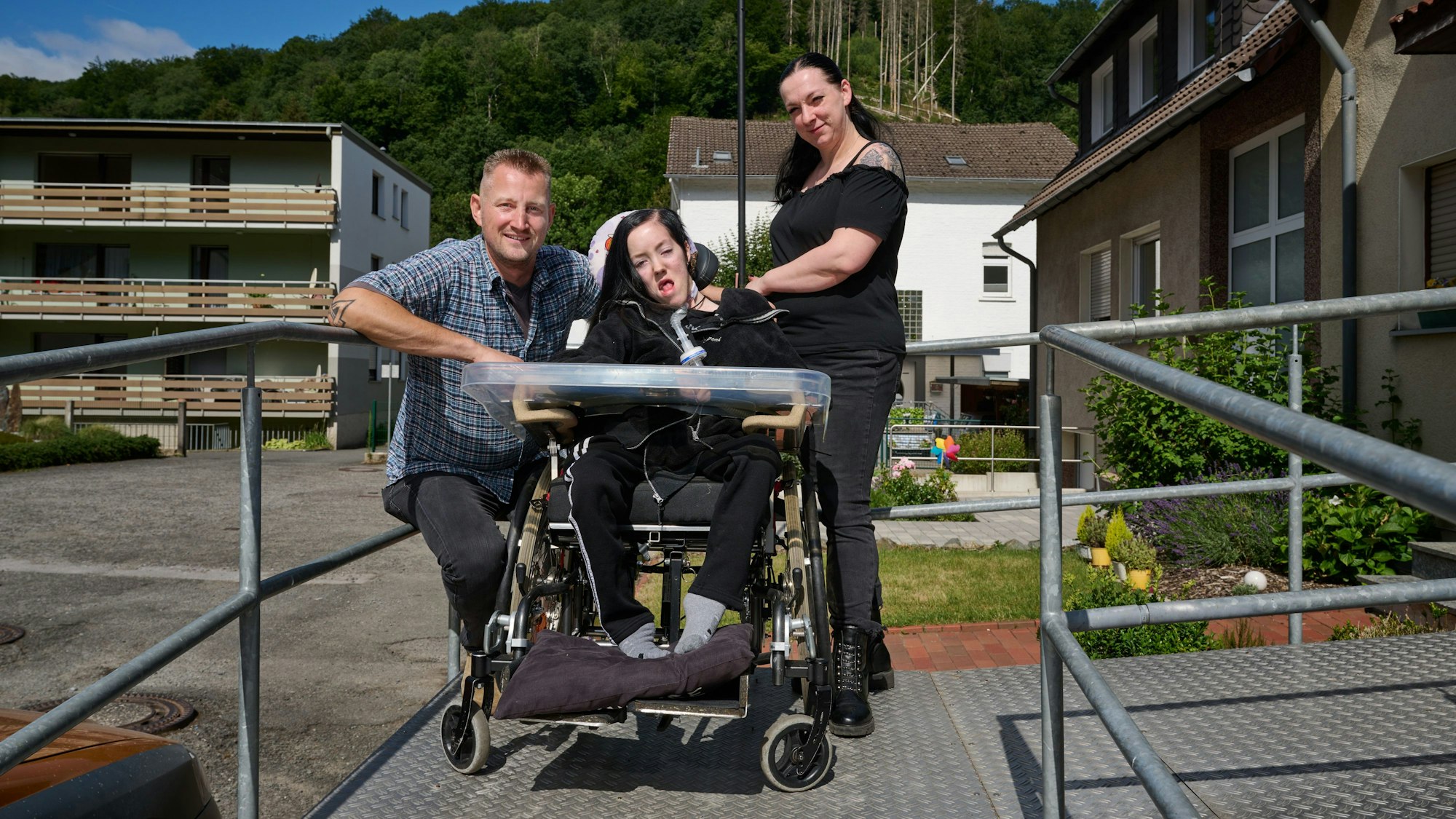 Dustin Raatz kniet neben dem Rollstuhl von Chantal und ihrer Mutter Bianca Caspari vor deren Haus. Mit einem tonnenschweren Bundeswehrfahrzeug aus dem Museum hatte Raatz das schwerkranke Mädchen während der schweren Flut im vergangenen Jahr gerettet und in Sicherheit gebracht, nachdem der letzte Akku ihres Beatmungsgerätes fast leer war.