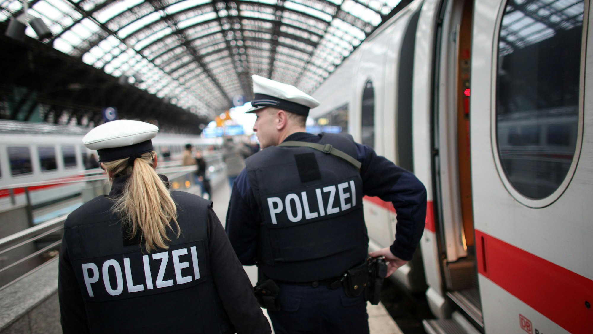 Zwei Einsatzkräfte der Bundespolizei gehen einen Bahnsteig im Kölner Hauptbahnhof entlang, neben ihnen steht ein ICE.