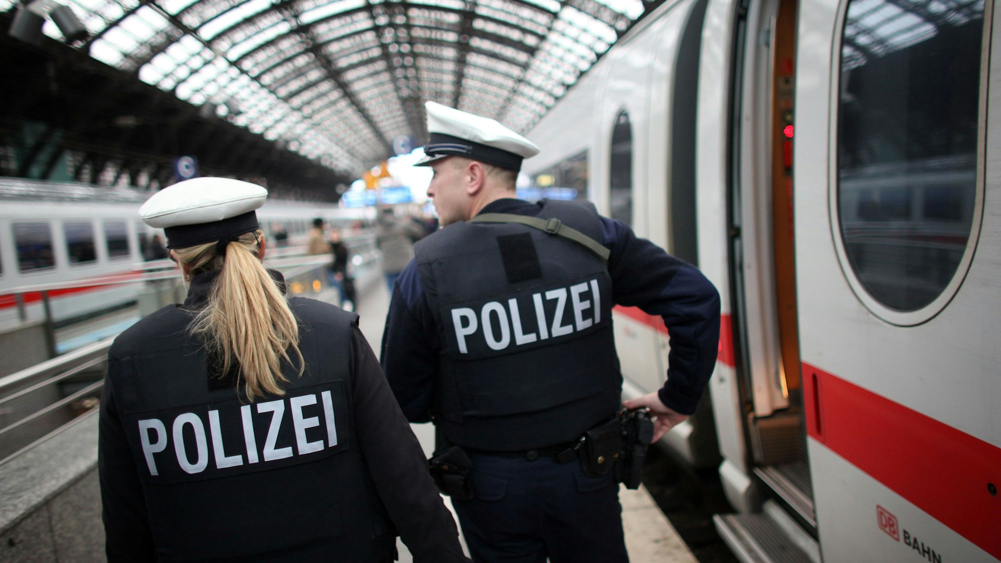 Eine Bundespolizistin und ein Bundespolizist patrouillieren auf einem Bahnsteig des Kölner Hauptbahnhofs, an dem ein ICE gehalten hat.