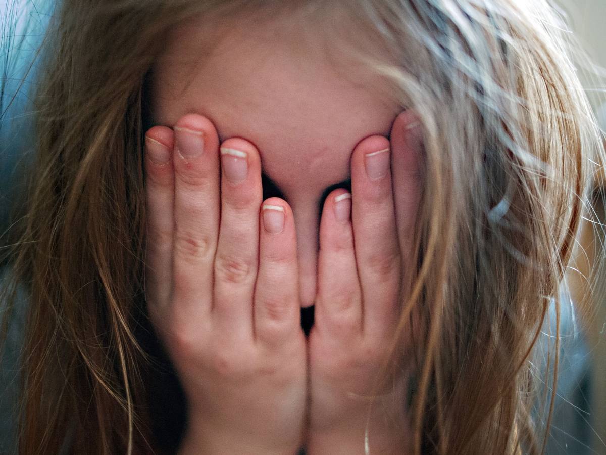 Auf dem Symbolfoto hält sich ein junges Mädchen die Hände vor ihr Gesicht.