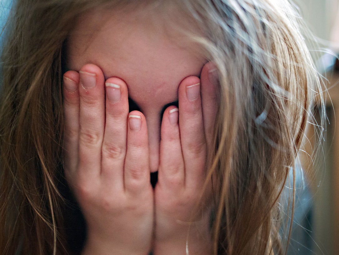 Auf dem Symbolfoto hält sich ein junges Mädchen die Hände vor ihr Gesicht.