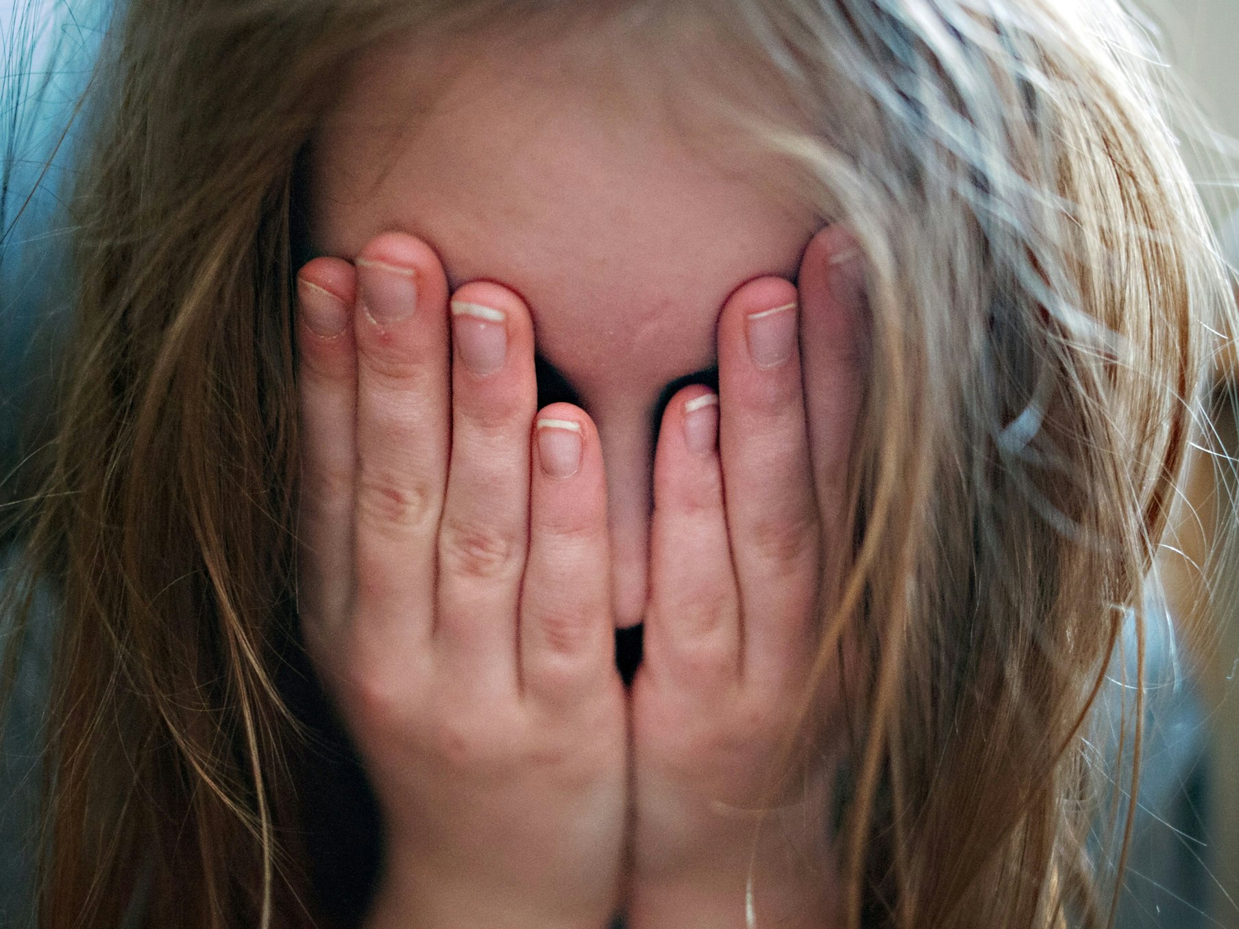 Auf dem Symbolfoto hält sich ein junges Mädchen die Hände vor ihr Gesicht.