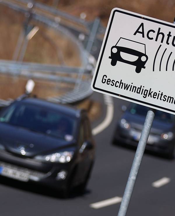 Autos fahren auf einer Landstraße an einem Warnschild für Geschwindigkeitsmessungen vorbei.