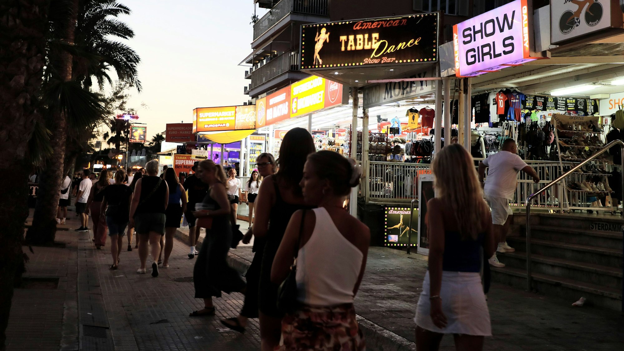 Palma: Menschen spazieren auf der Strandpromenade von Arenal auf Mallorca an Show-Bars vorbei.
