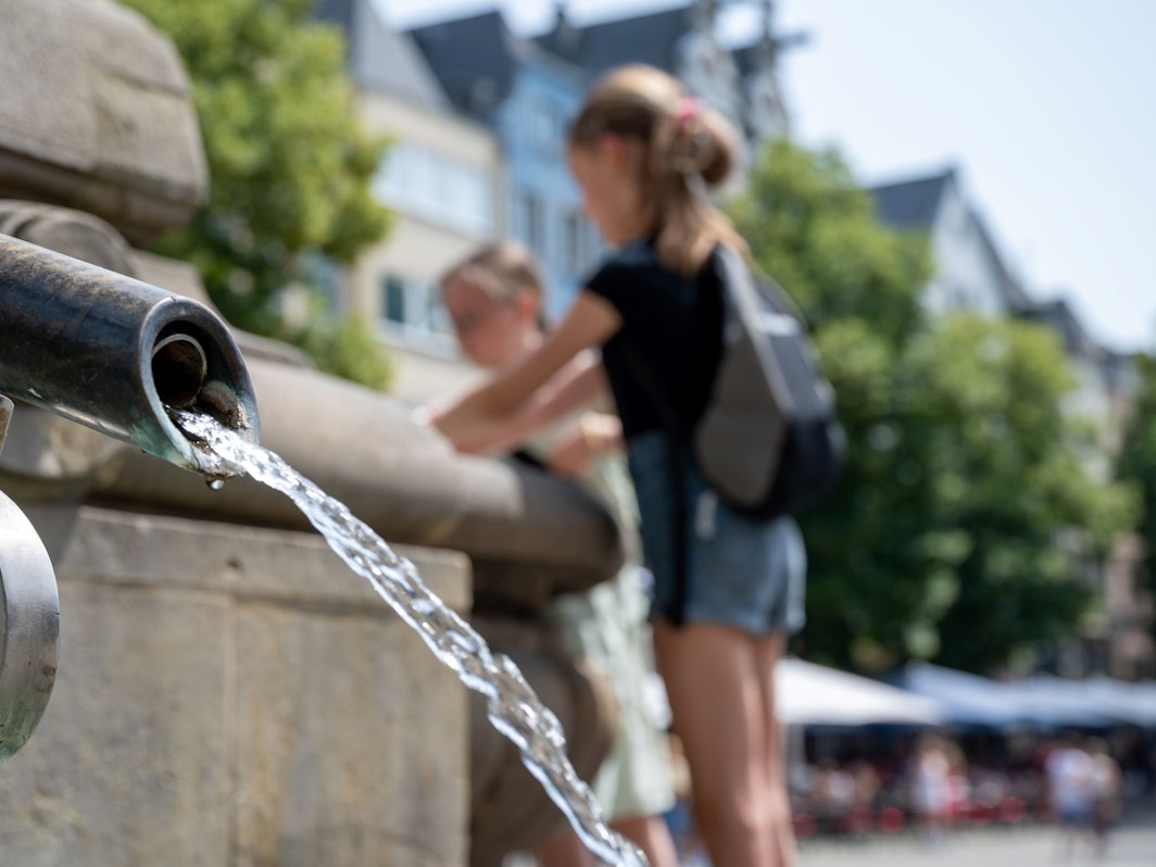 Eine Kölnerin kühlt sich an einem Brunnen in der Altstadt ab.
