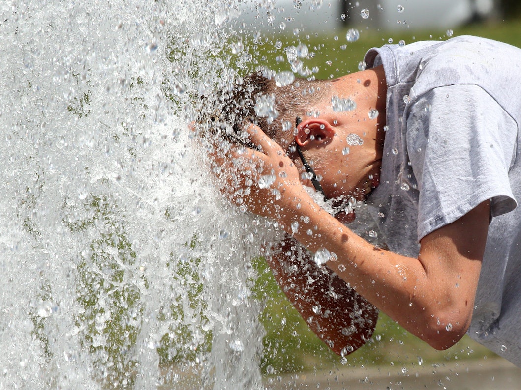 Ein Mann erfrischt sich an einem Brunnen in Berlin.
