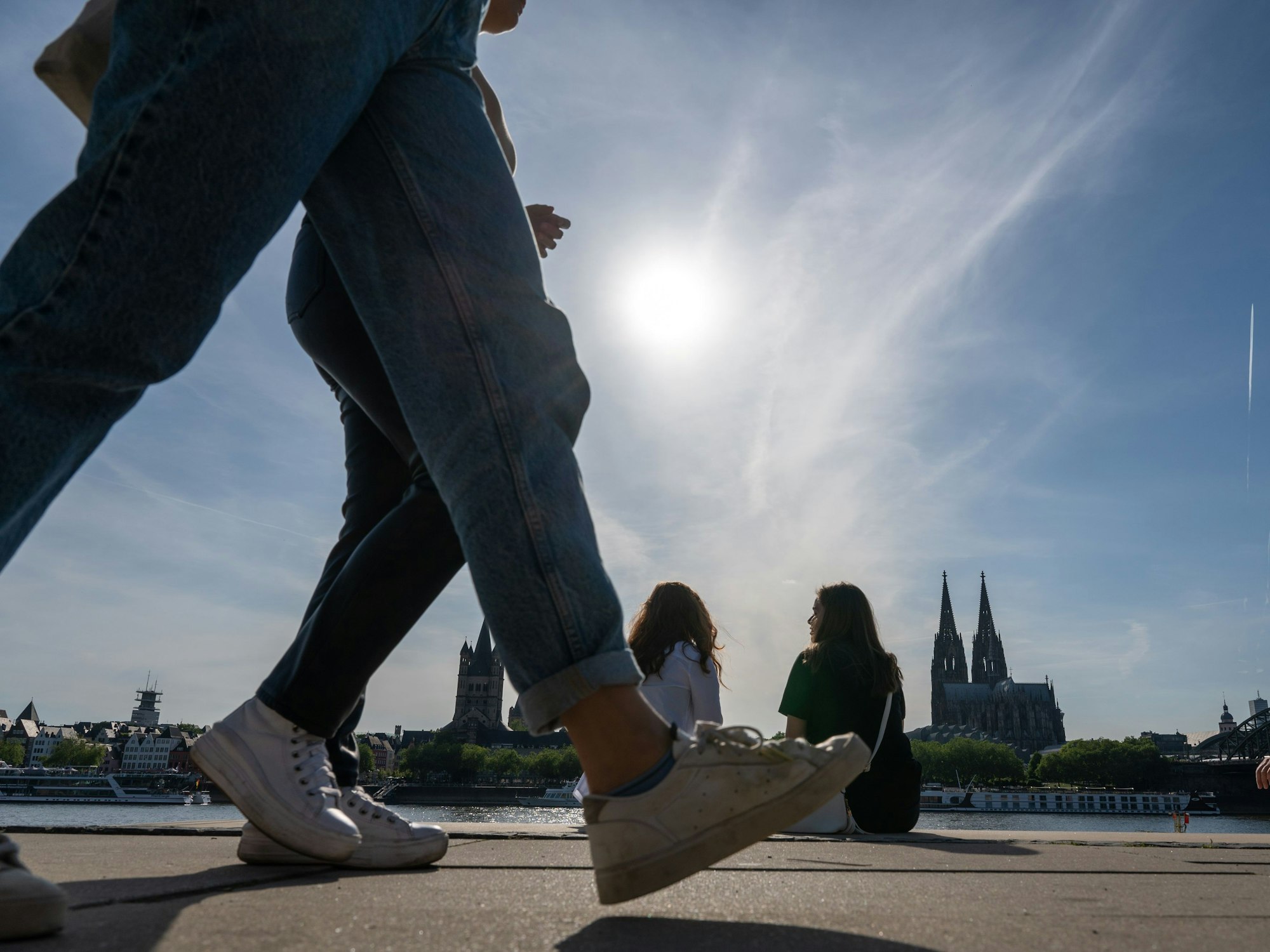 Am Rheinboulevard flanieren junge Leute durch den Sonnenschein.