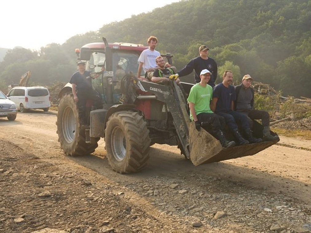 Helfer der Flutkatastrophe in NRW und Rheinland-Pfalz sitzen auf einem Bagger.