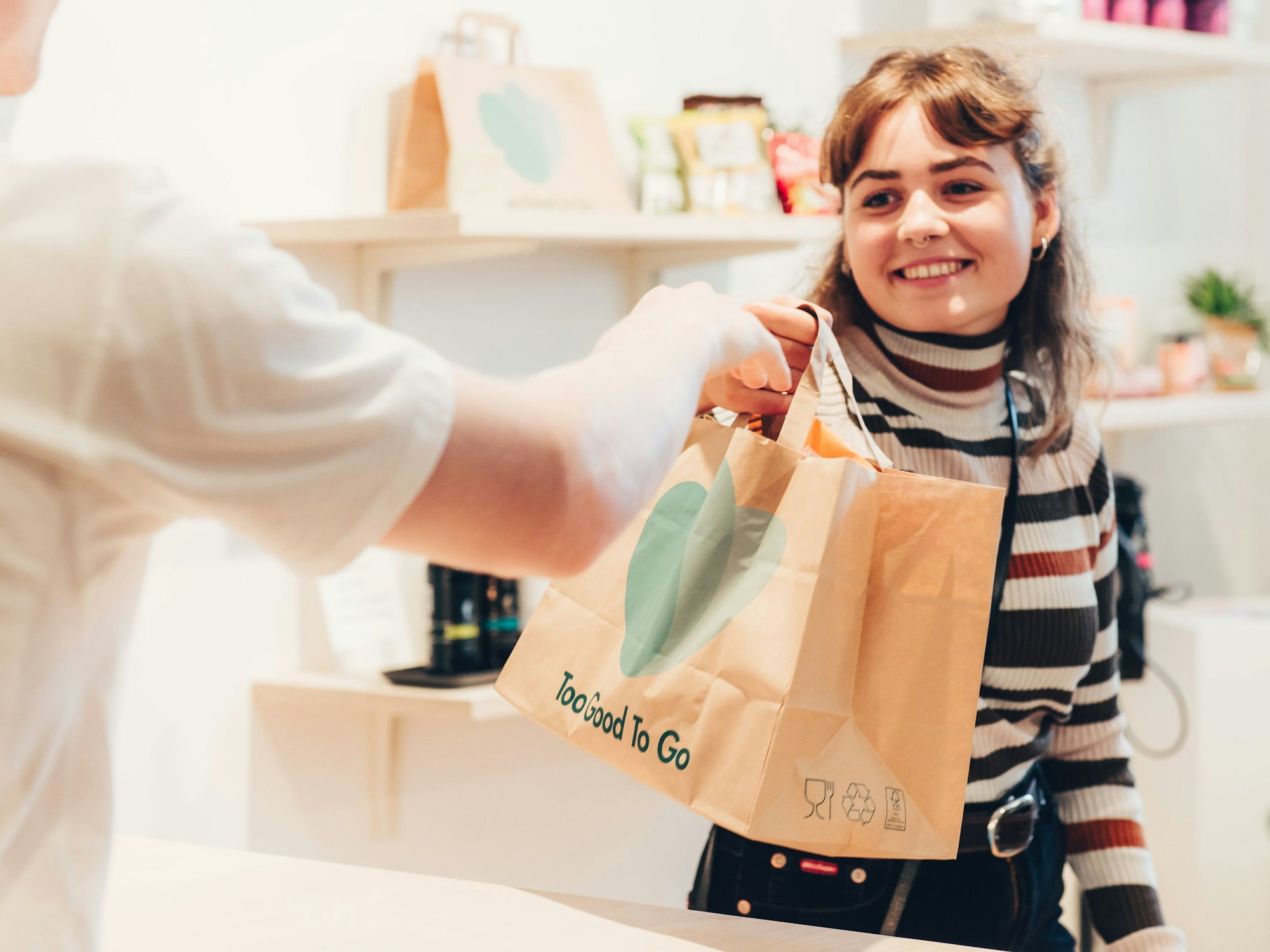 Eine Kundin bekommt eine „Too Good To Go“-Tüte überreicht.