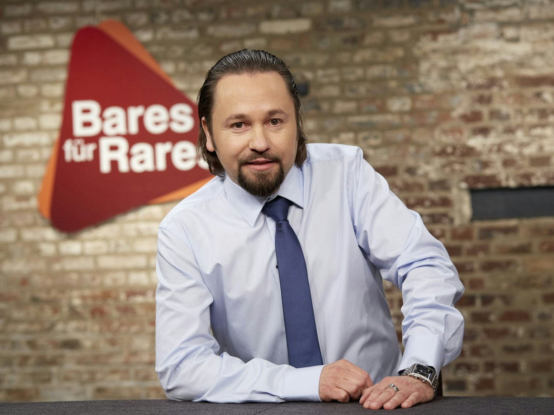 „Bares für Rares“-Händler Wolfgang Pauritsch posiert in der Kulisse der Show für ein Pressefoto.