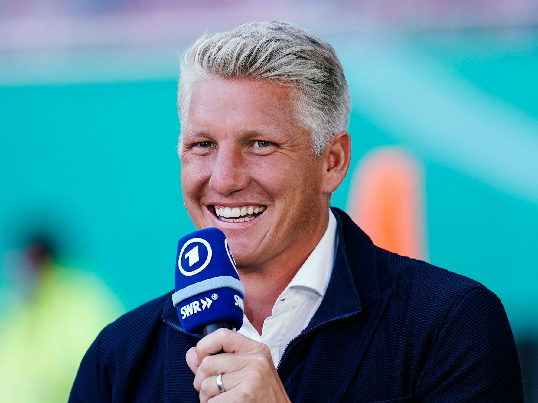 Bastian Schweinsteiger, TV-Experte der ARD, lacht mit einem Mikrofon in der Hand.