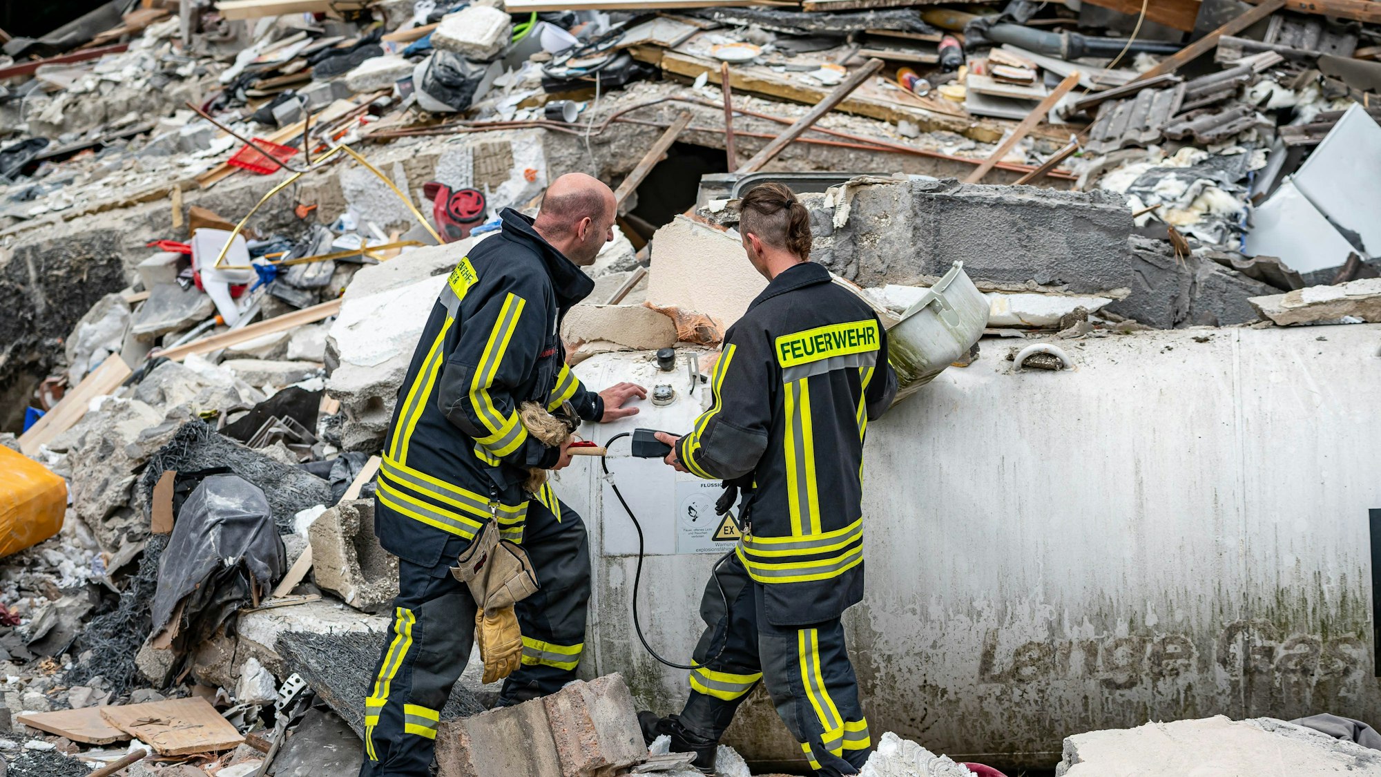 Feuerwehrleute machen eine Messung an einem Gastank zwischen den Trümmern nach einer Hausexplosion in Hemer.