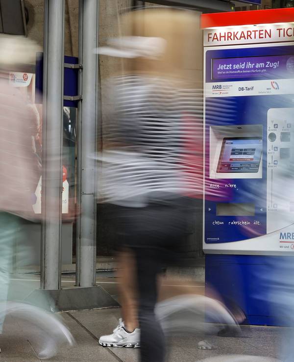 Reisende gehen an einem Fahrkartenautomaten vorbei