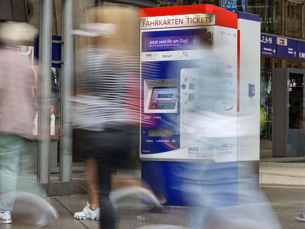 Reisende gehen an einem Fahrkartenautomaten vorbei