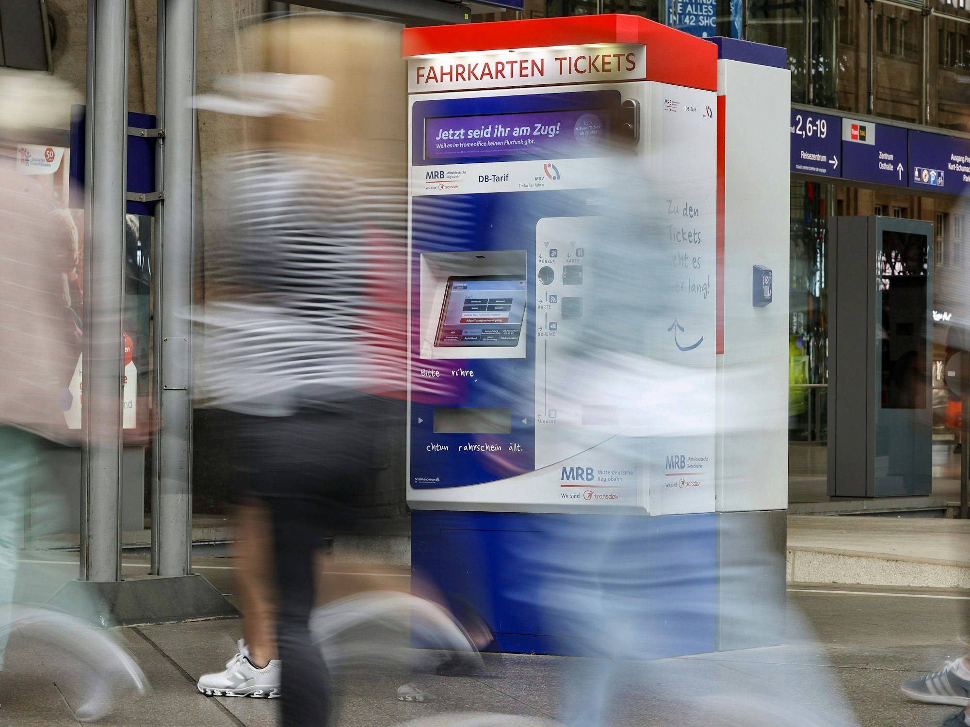 Reisende gehen an einem Fahrkartenautomaten vorbei