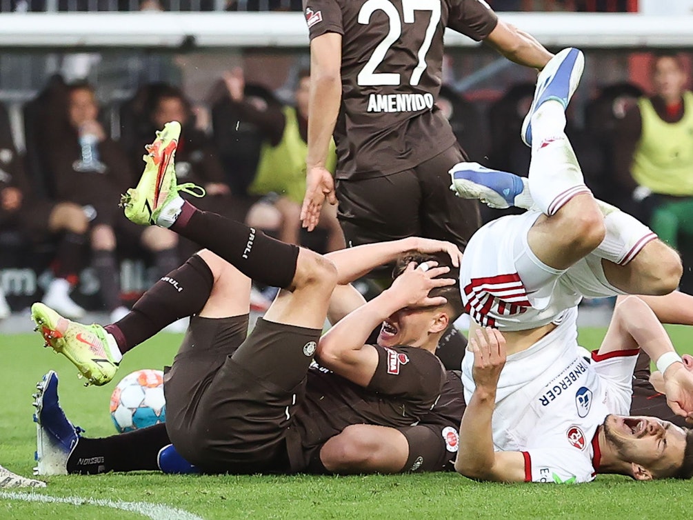 Spieler vom FC St. Pauli und vom 1. FC Nürnberg liegen nach einem Zusammenstoß auf dem Rasen.