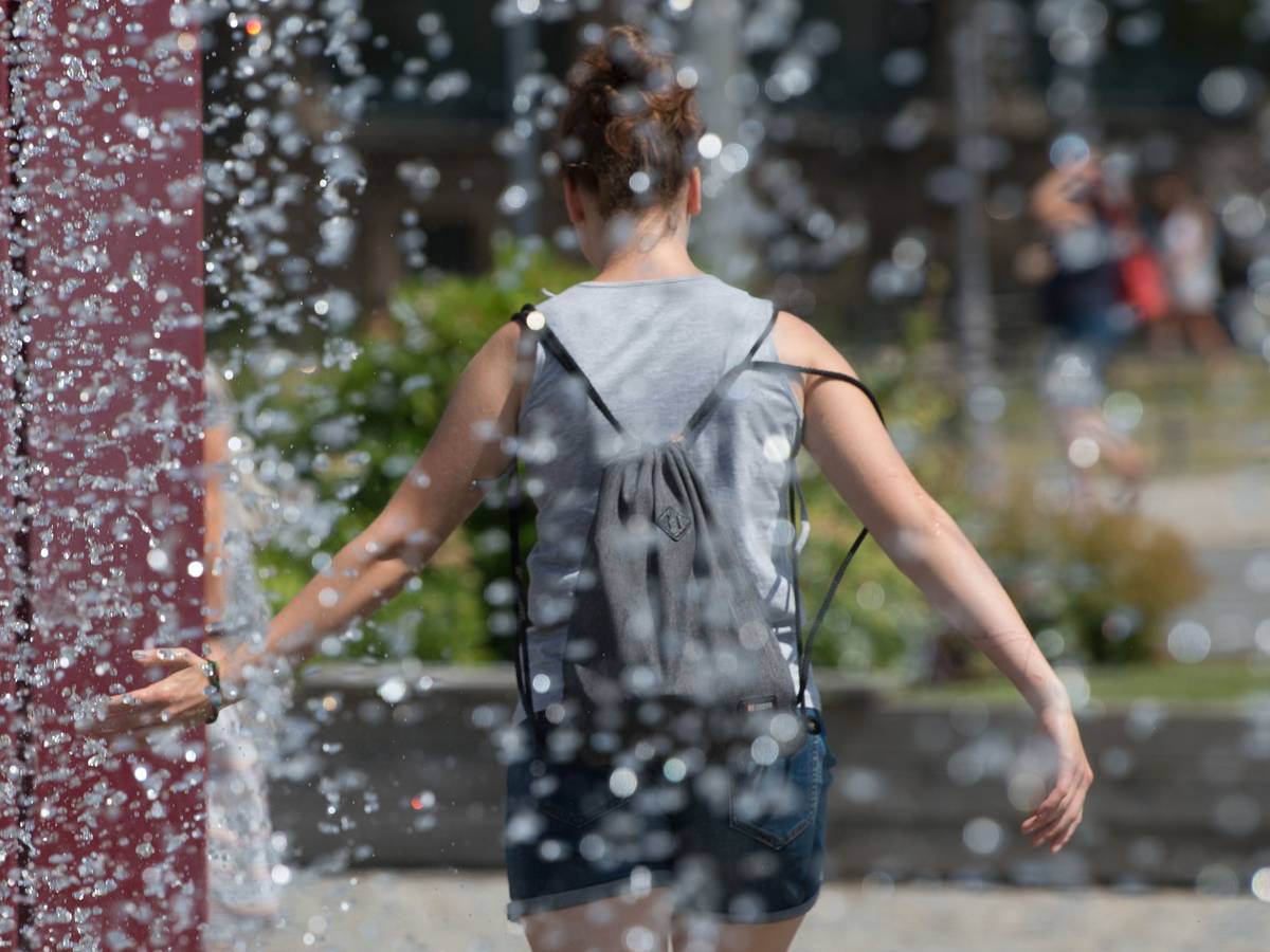 Eine Frau kühlt sich an einem Springbrunnen ab.