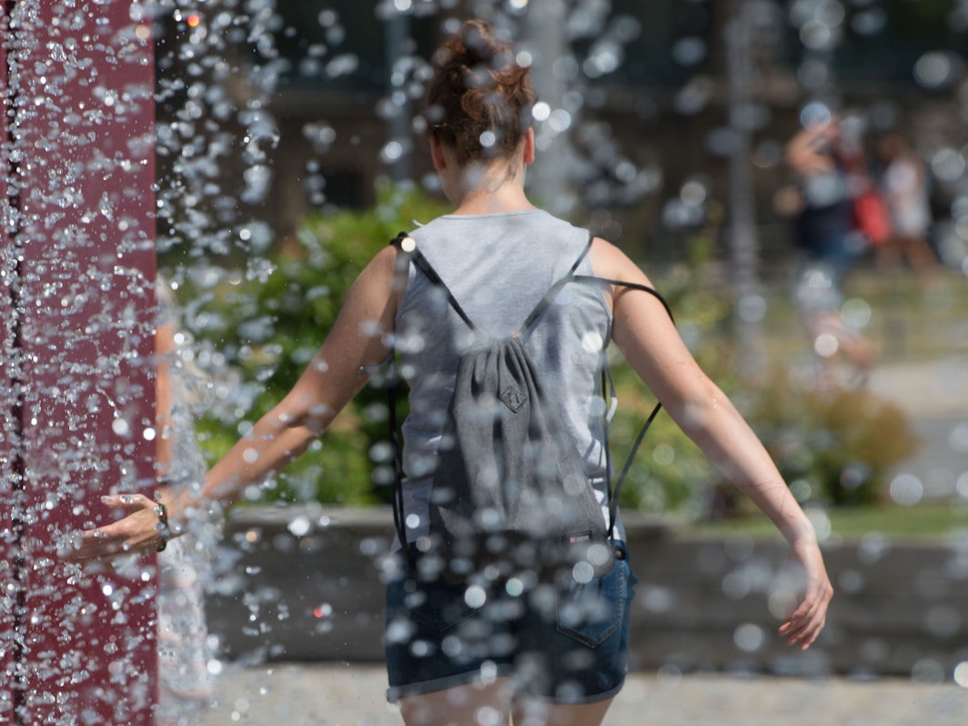 Eine Frau kühlt sich an einem Springbrunnen ab.